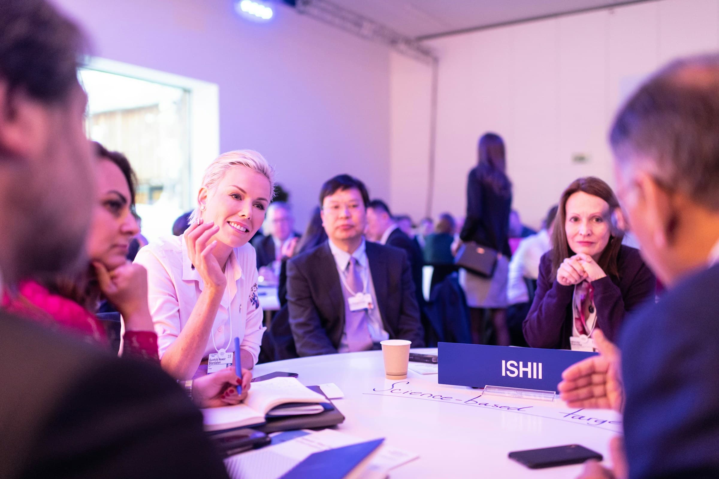 Professionals wearing name badges in discussion around a table at a conference.
