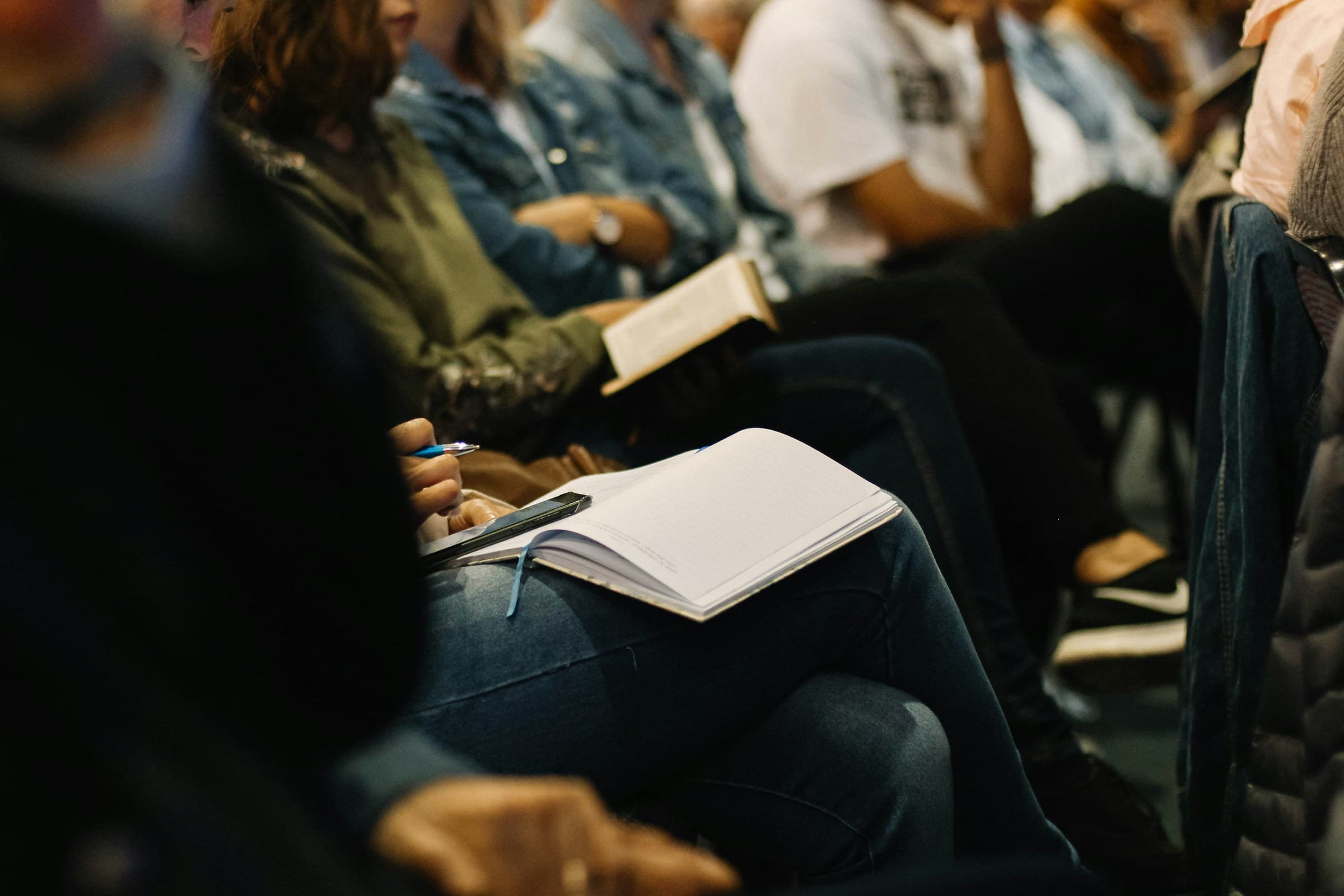 Delegates seated in a row taking notes in open notebooks during a session.